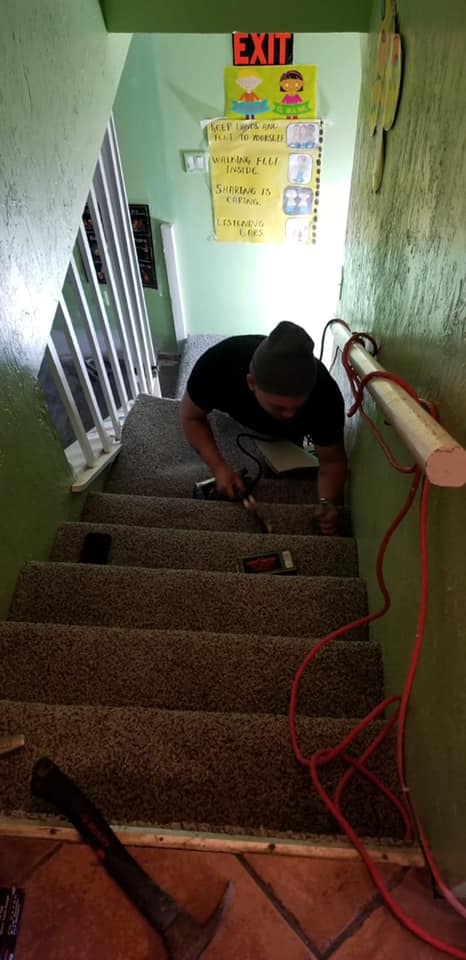 Contractor installing gray carpet on stairwell covered in green walls.