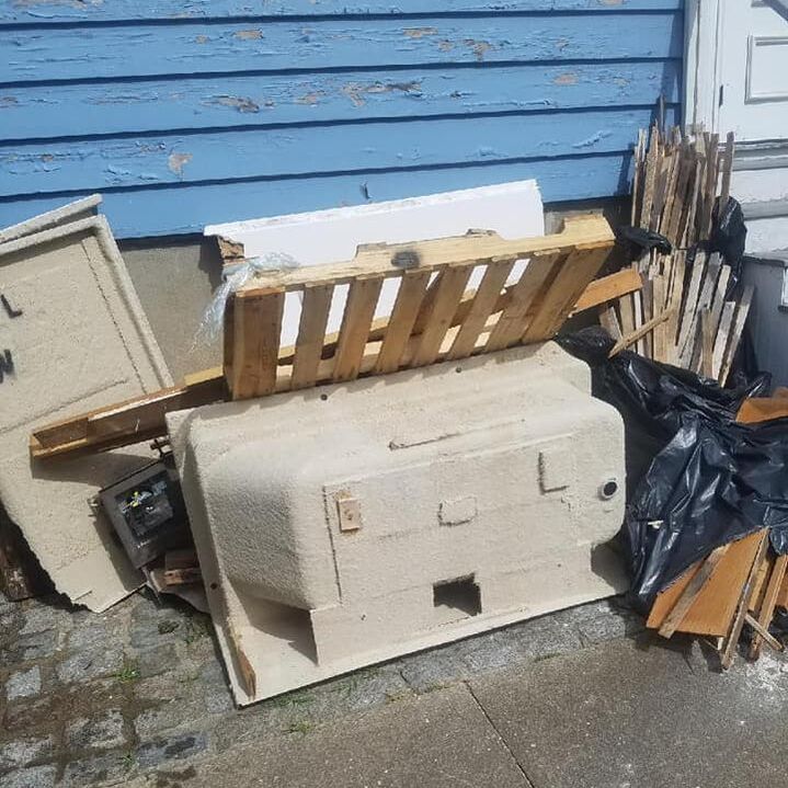 Pile of pallet and appliance packaging and debris from renovation sitting outside on side of blue house.