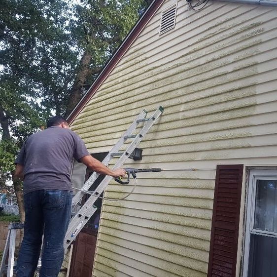 Contractor power washing dirty siding of beige house with brown shutters
