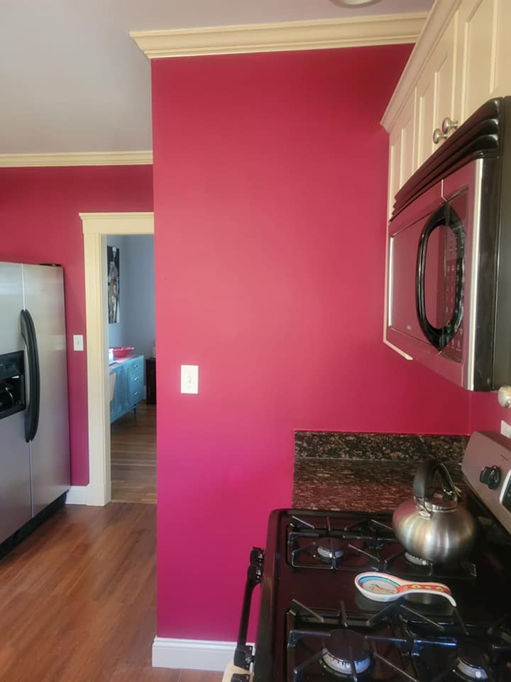 Newly painted red walls with white trim in kitchen. View of stainless steel refrigerator, black marble counter, stove top and microwave.