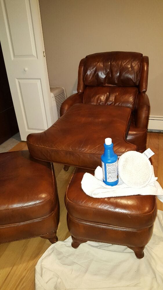 Brown leather lounge chair with ottoman being cleaned and buffed with blue leather chair cleaner and buffing pad.