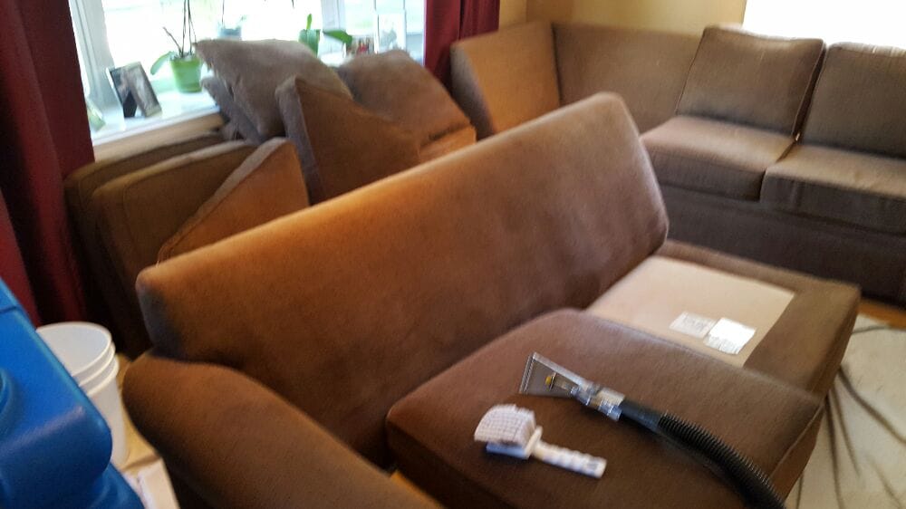 Brown sectional sofa being steam cleaned with upholstery hose and scrub brush.